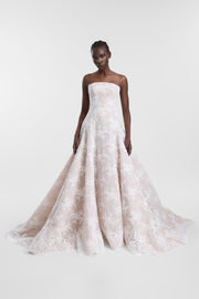A model wearing a strapless A-line wedding gown in a pale blush pink lace, standing against a light gray studio background.
