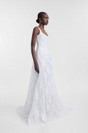A woman modeling a sleeveless white lace wedding gown in a side-profile pose against a clean, light gray studio background.