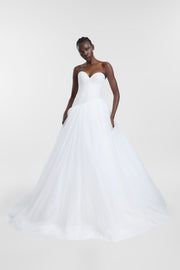A model wearing a strapless white wedding gown with a sweetheart neckline, structured bodice, and a voluminous tulle skirt, photographed against a seamless light gray studio background.