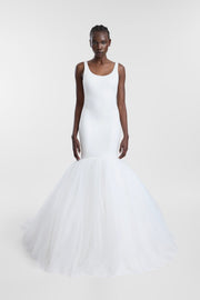 A model wearing a white sleeveless mermaid-style gown with a fitted bodice and a voluminous tulle skirt, photographed against a plain light gray studio background.