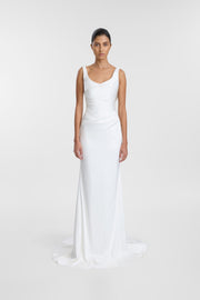 A woman modeling a sleeveless white satin gown with a V-neckline and a floor-length silhouette, photographed against a seamless light gray studio background.