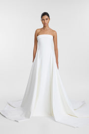 A model wearing a strapless white wedding gown with a structured bodice with foldover detail and a long flowing train, photographed against a clean light gray studio background.
