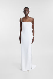 A model wearing a floor-length white slip dress with thin shoulder straps and side tie details, photographed against a seamless light gray studio background.