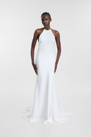 A model wearing a white halter-neck floor-length gown with a slight train, photographed against a seamless light gray studio background.