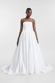 A model wearing a strapless white ball gown with a structured bodice and a full, flowing skirt, photographed against a light gray studio background.