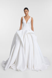 A model wearing a white bridal gown with a deep V-neckline, sleeveless straps, and a voluminous layered tulle skirt, photographed against a seamless light gray studio background.